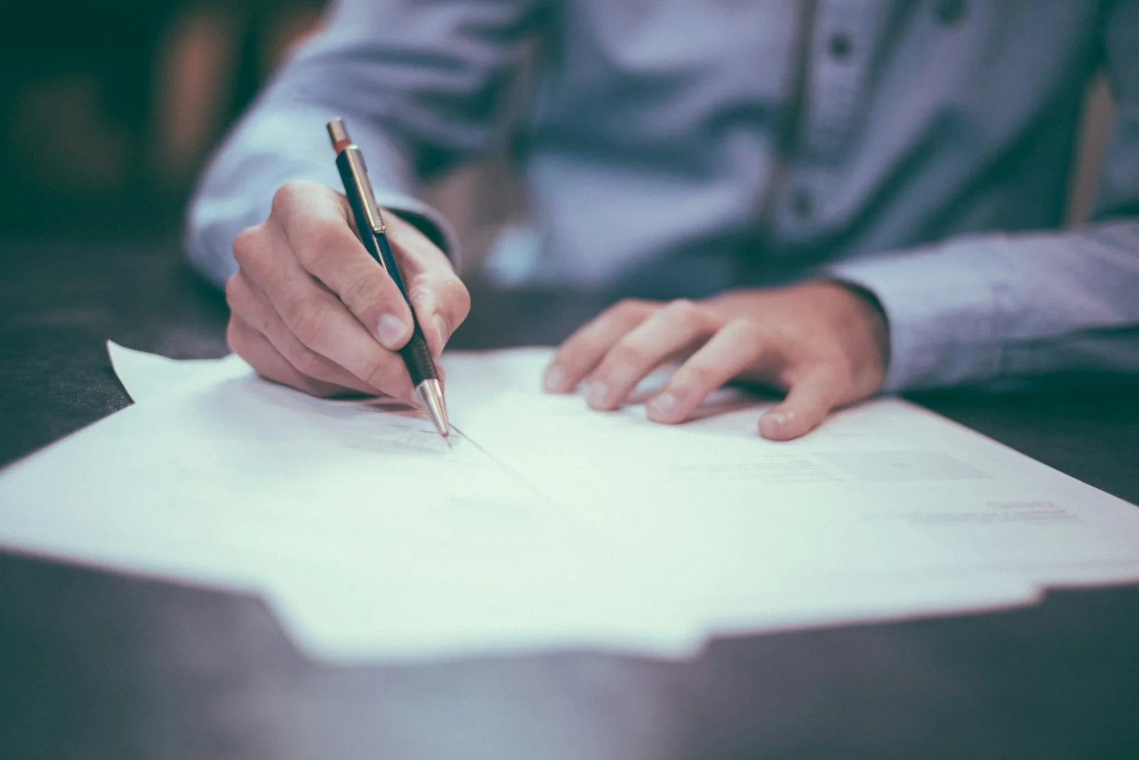 A person reviewing and signing paperwork at a desk.