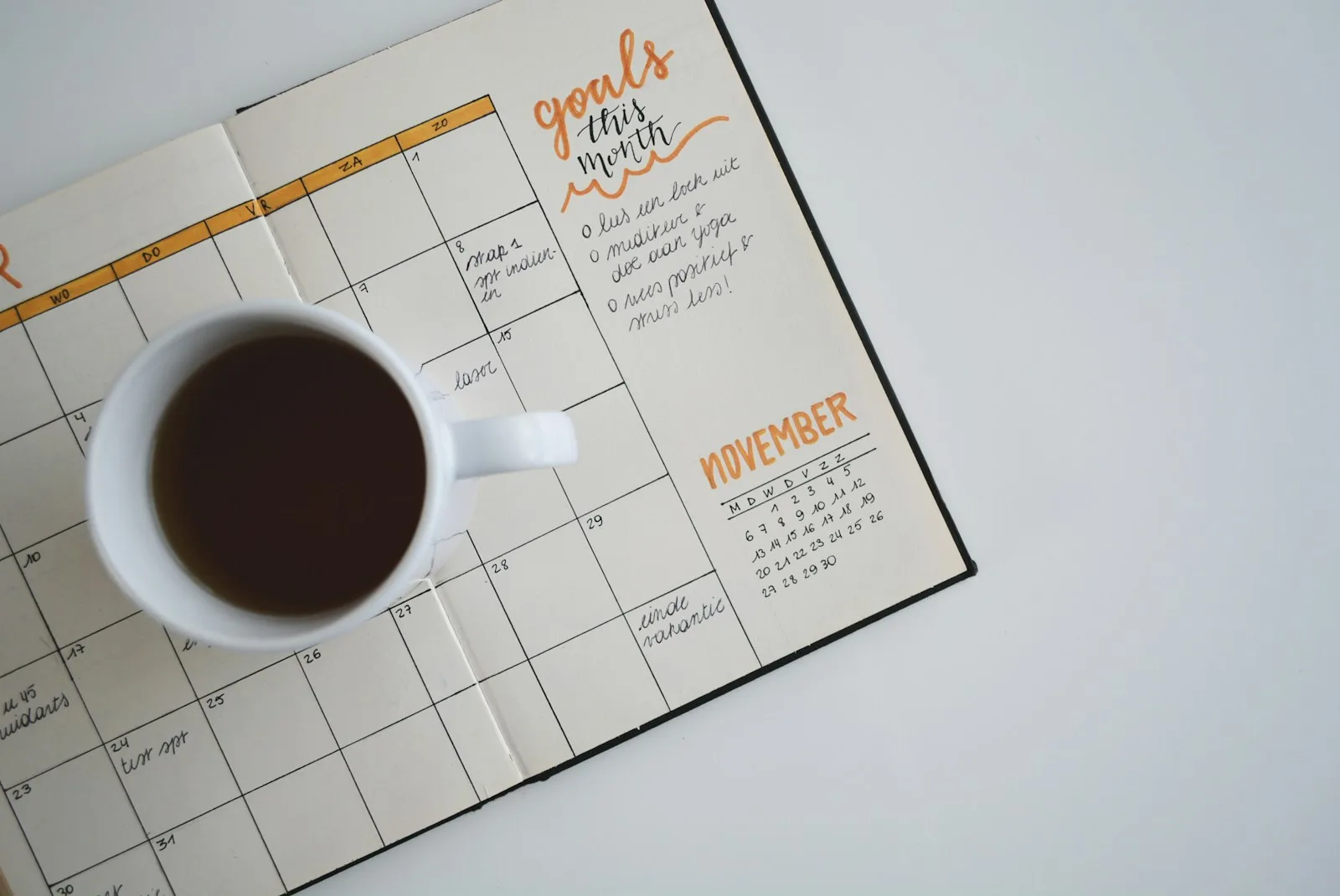 A handwritten monthly planner with a cup of coffee on a light desk.